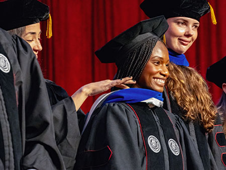 A graduate student receiving their doctoral hood during a ceremony.